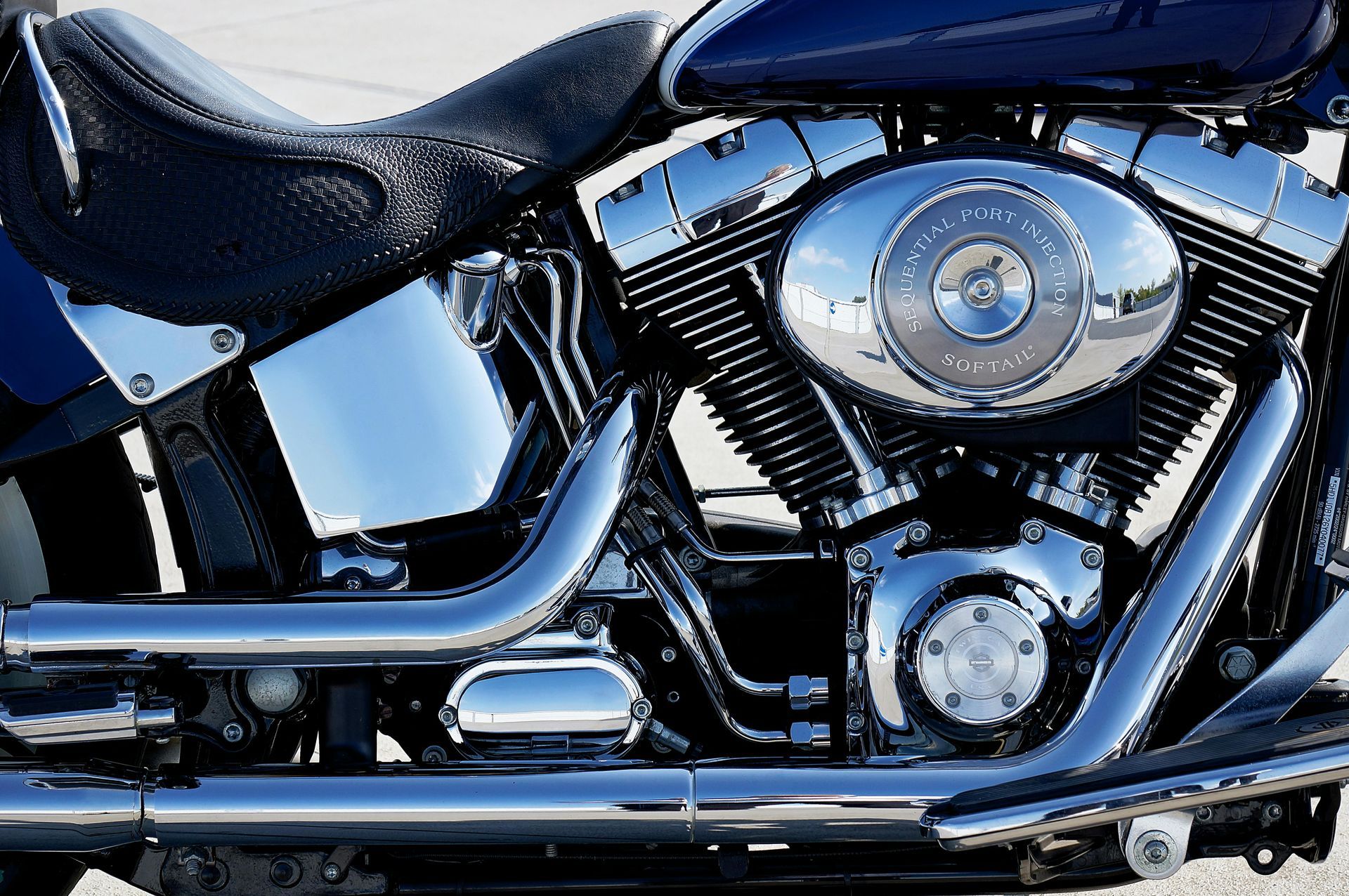 Close-up of a chrome motorcycle engine and black leather seat on a dark blue bike