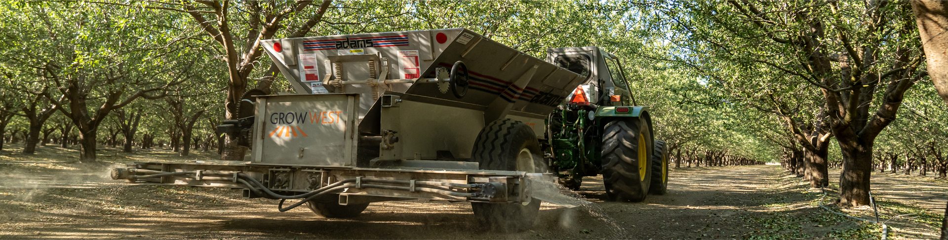 A tractor pulling a fertilizer spreader in an orchard.