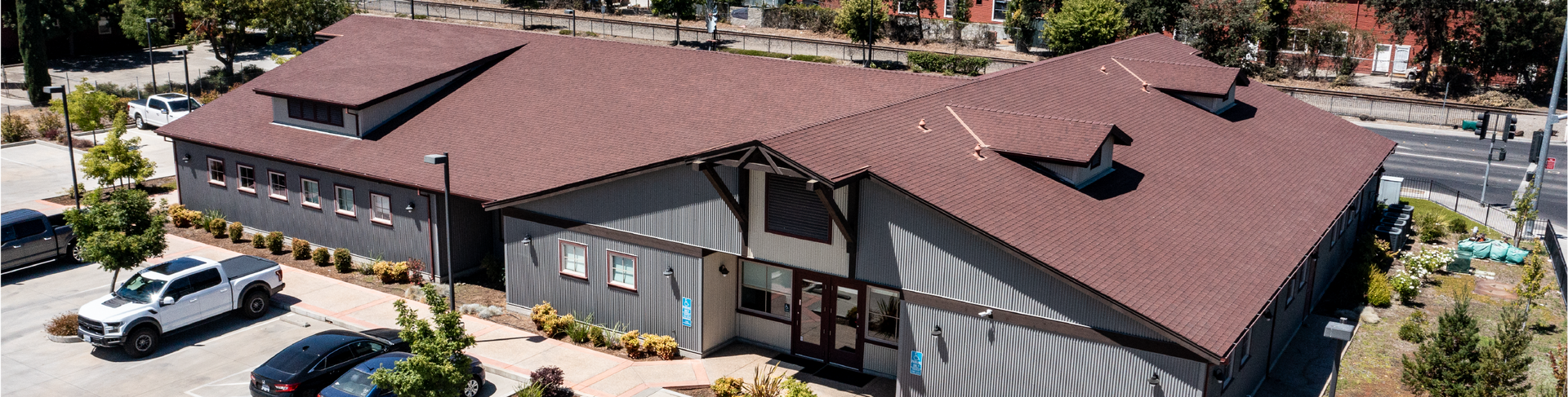 Building with a brown roof and gray siding. Cars parked in front.