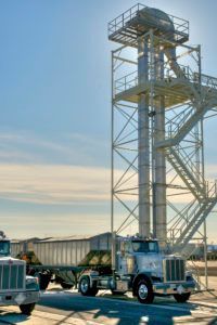 Truck loading grain at an industrial elevator against a blue sky.