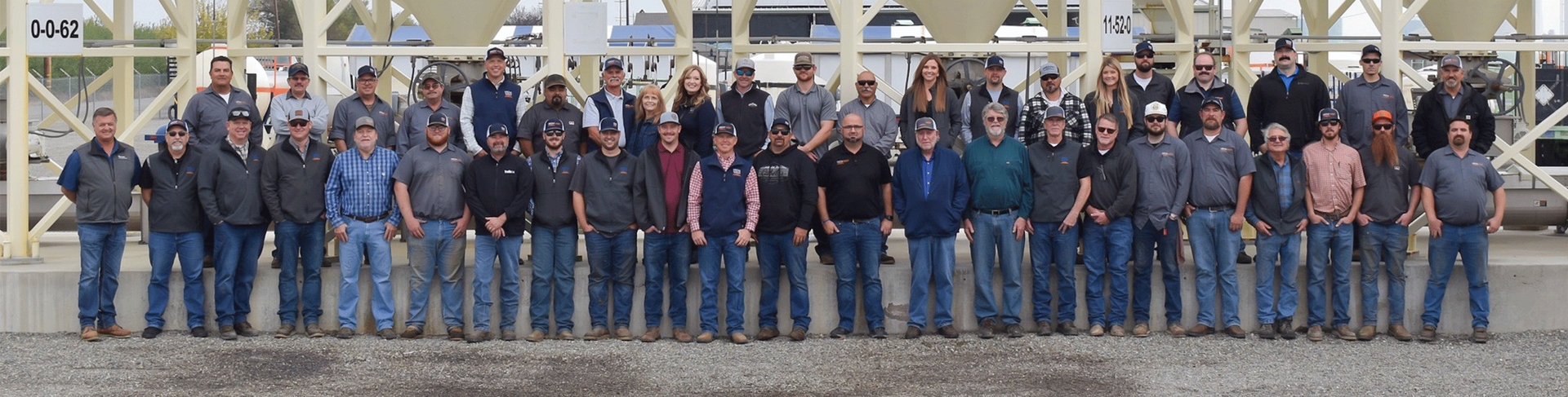 Group of people standing outdoors, wearing jeans and jackets, posing for a photo.