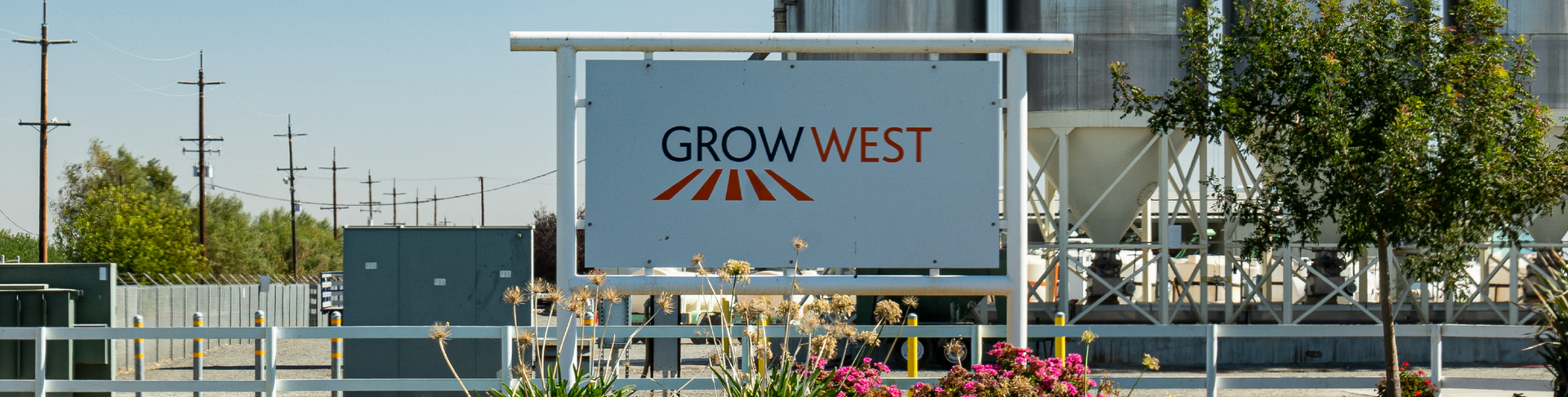 Sign for Grow West with red and orange logo, set in front of a building and greenery.