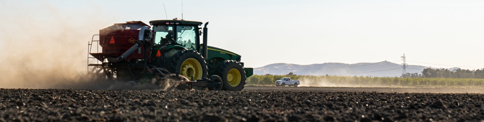 Green tractor plowing a field on a sunny day, kicking up dust.