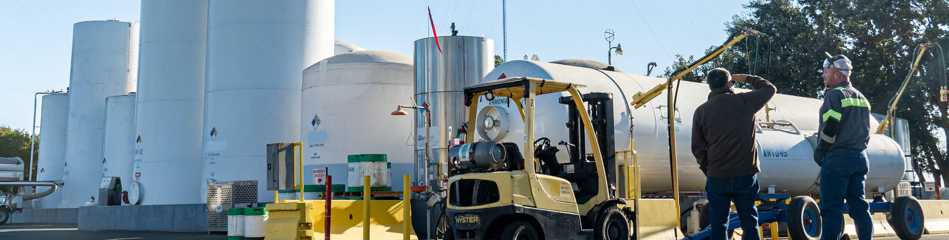 Forklift near large tanks, workers by a cylindrical tank, industrial setting.