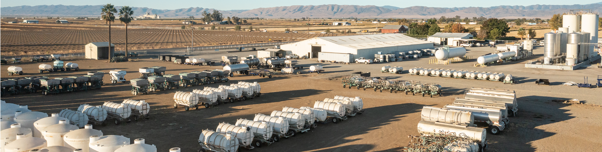 A dry, dusty industrial landscape with white tanks and buildings. In the background are hills and sky.