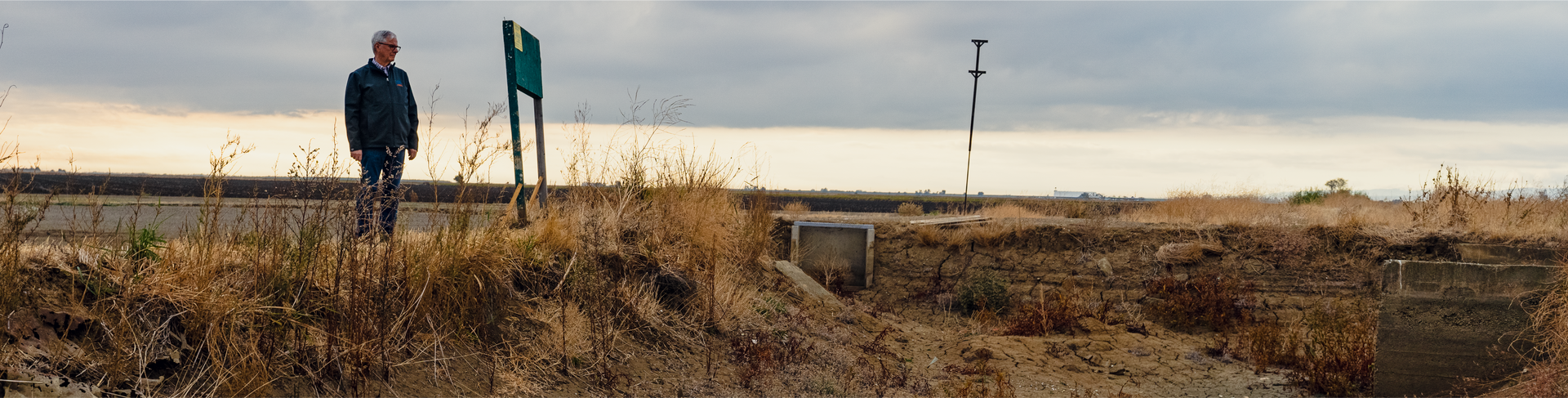 Person standing near a sign on a grassy plain under an overcast sky.