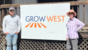 Two people stand in front of a white sign with