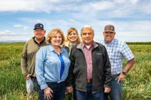 Five people in a field smiling, cloudy sky; two women, three men; outdoors.