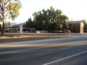 Roadside farm stand with covered area, trees, a barn, and a tractor.