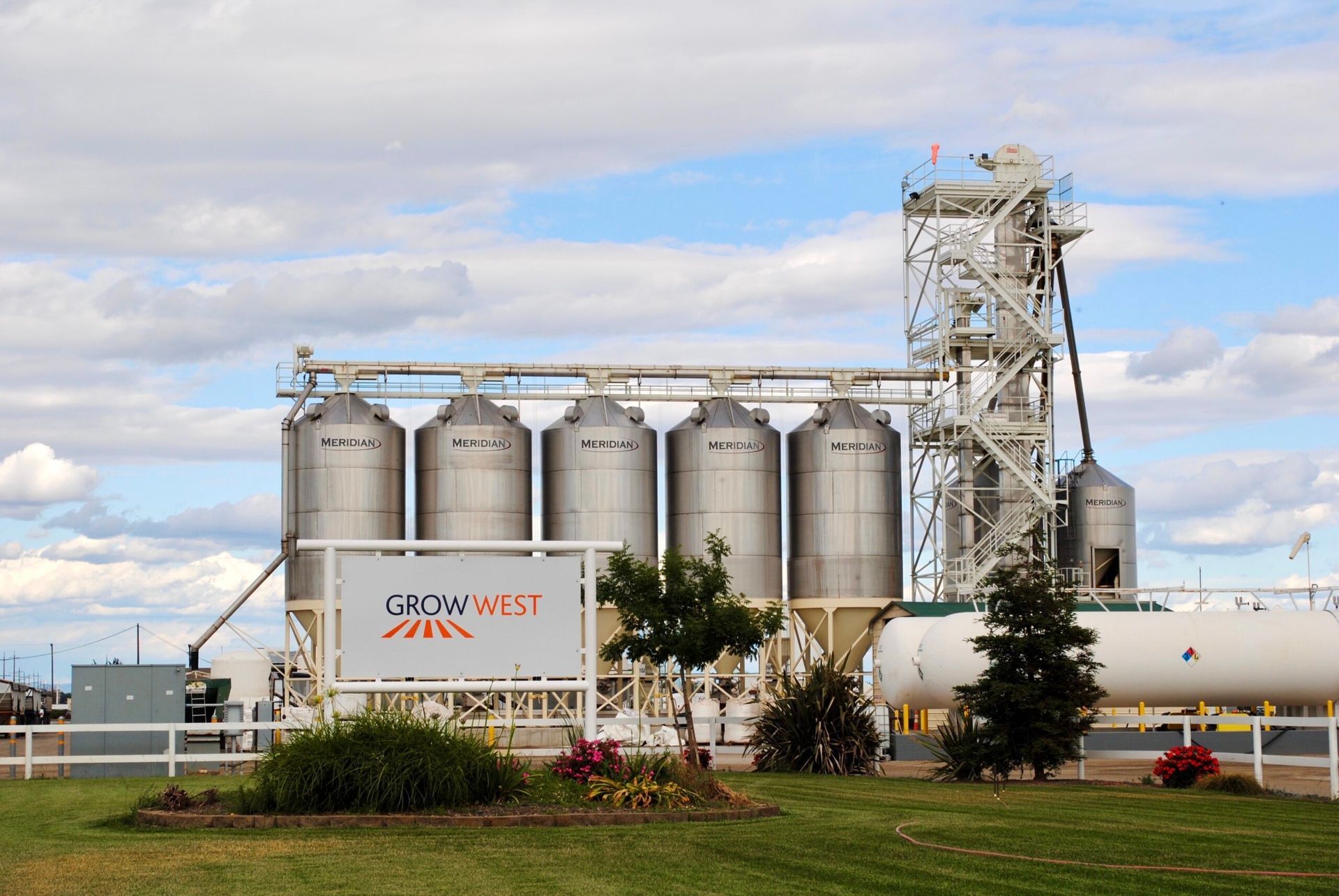Grain silos with the Grow West logo, under a partly cloudy sky.