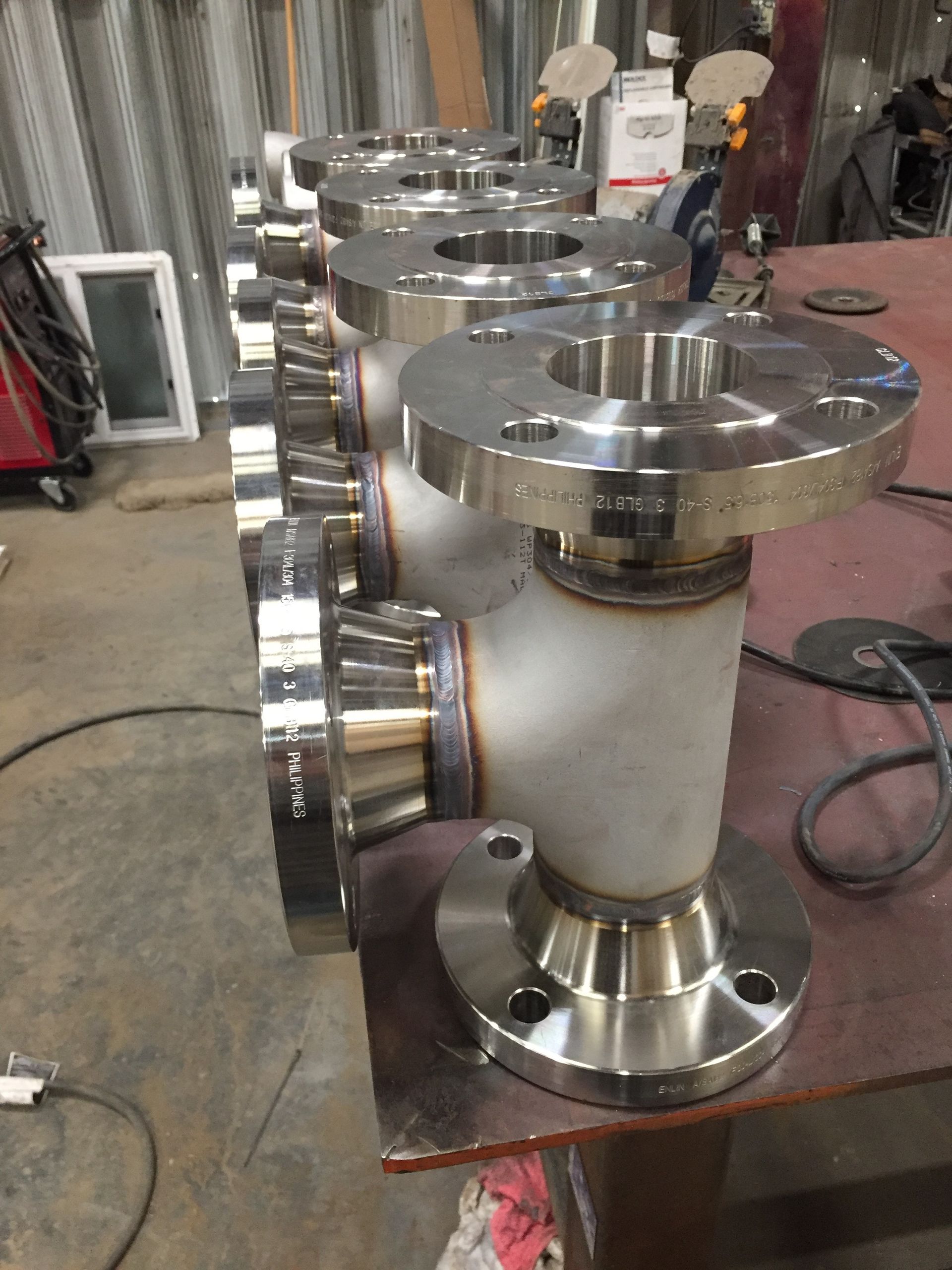 Row of stainless steel industrial flanged pipe fittings on a workshop table
