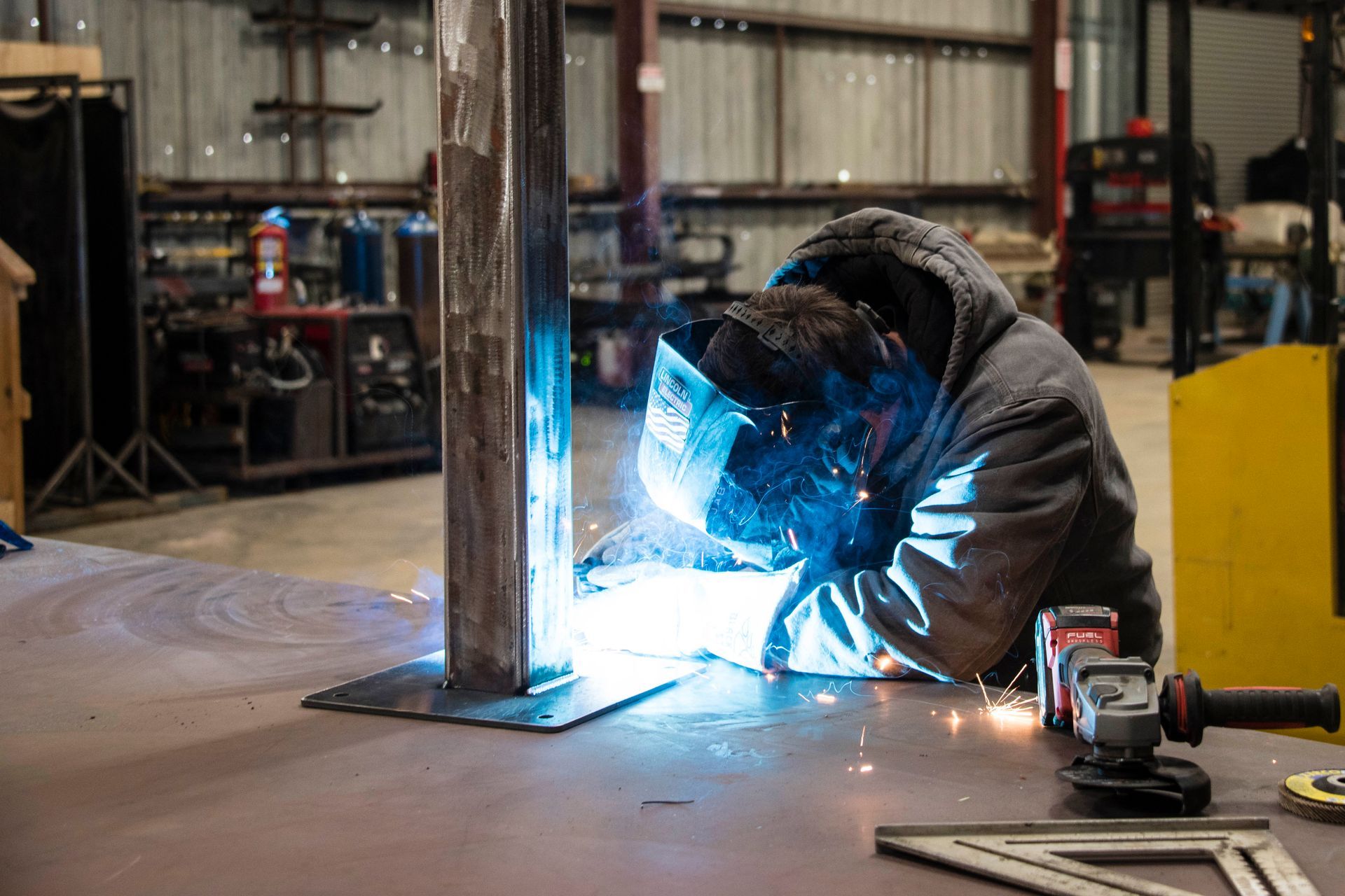 Welder in protective gear welding a metal frame, bright blue sparks in a workshop