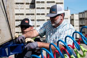 Two men in caps, wearing gloves, working on a truck. Blue, red air hoses. Gray background.