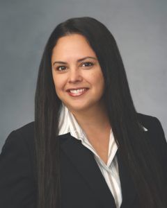 Woman with long dark hair, wearing a dark suit jacket over a striped blouse, smiling.