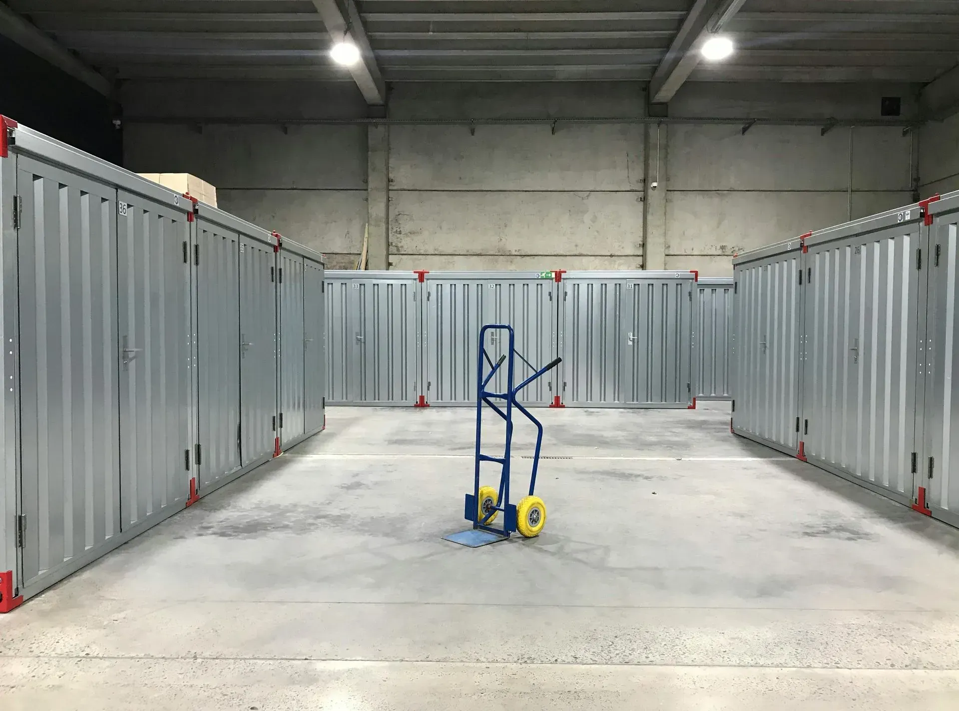 Industrial warehouse aisle with gray storage units and a blue hand truck centered on the floor.