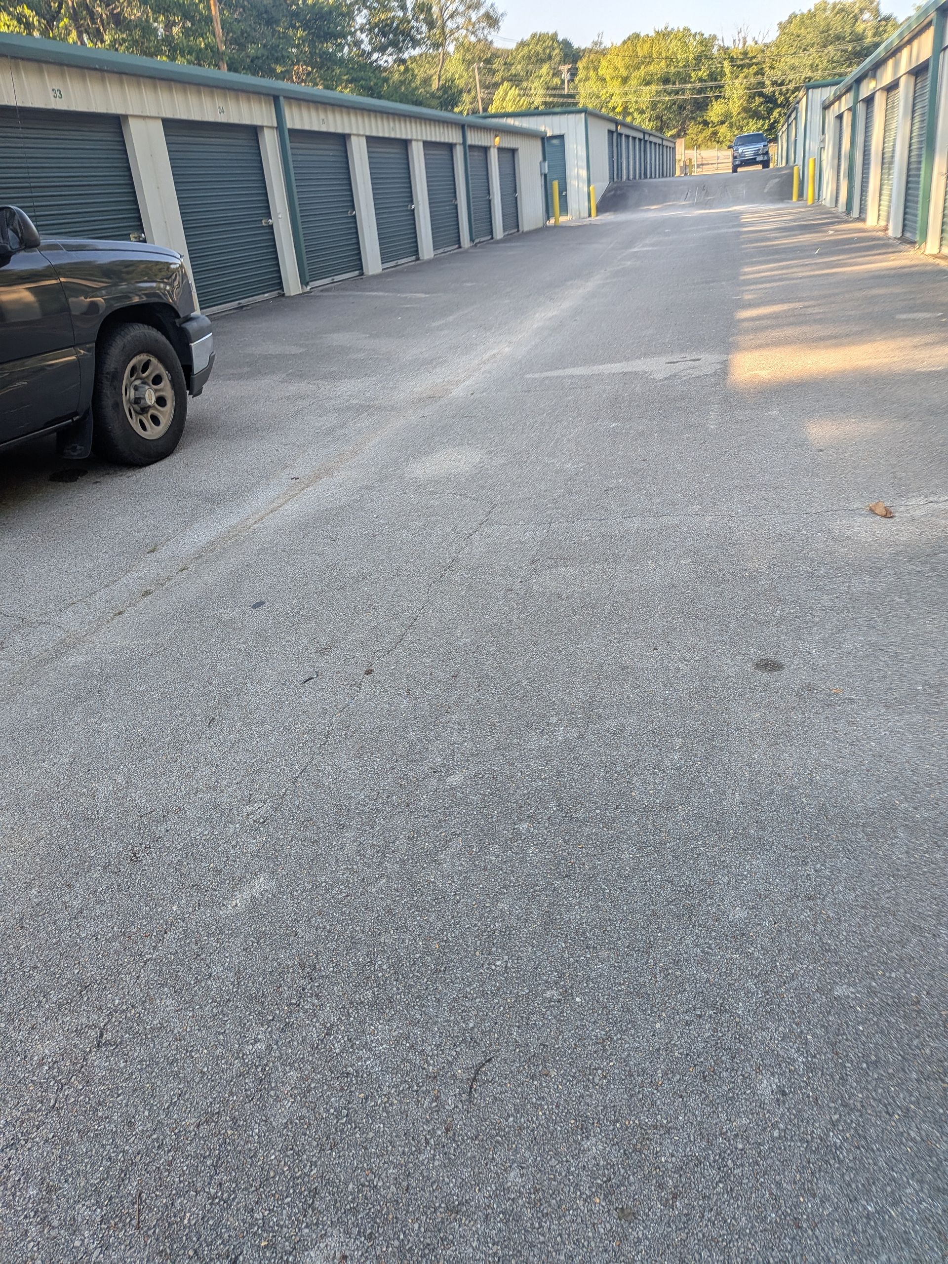 Gravel driveway between rows of blue-gray storage units, with a black truck parked on the left.