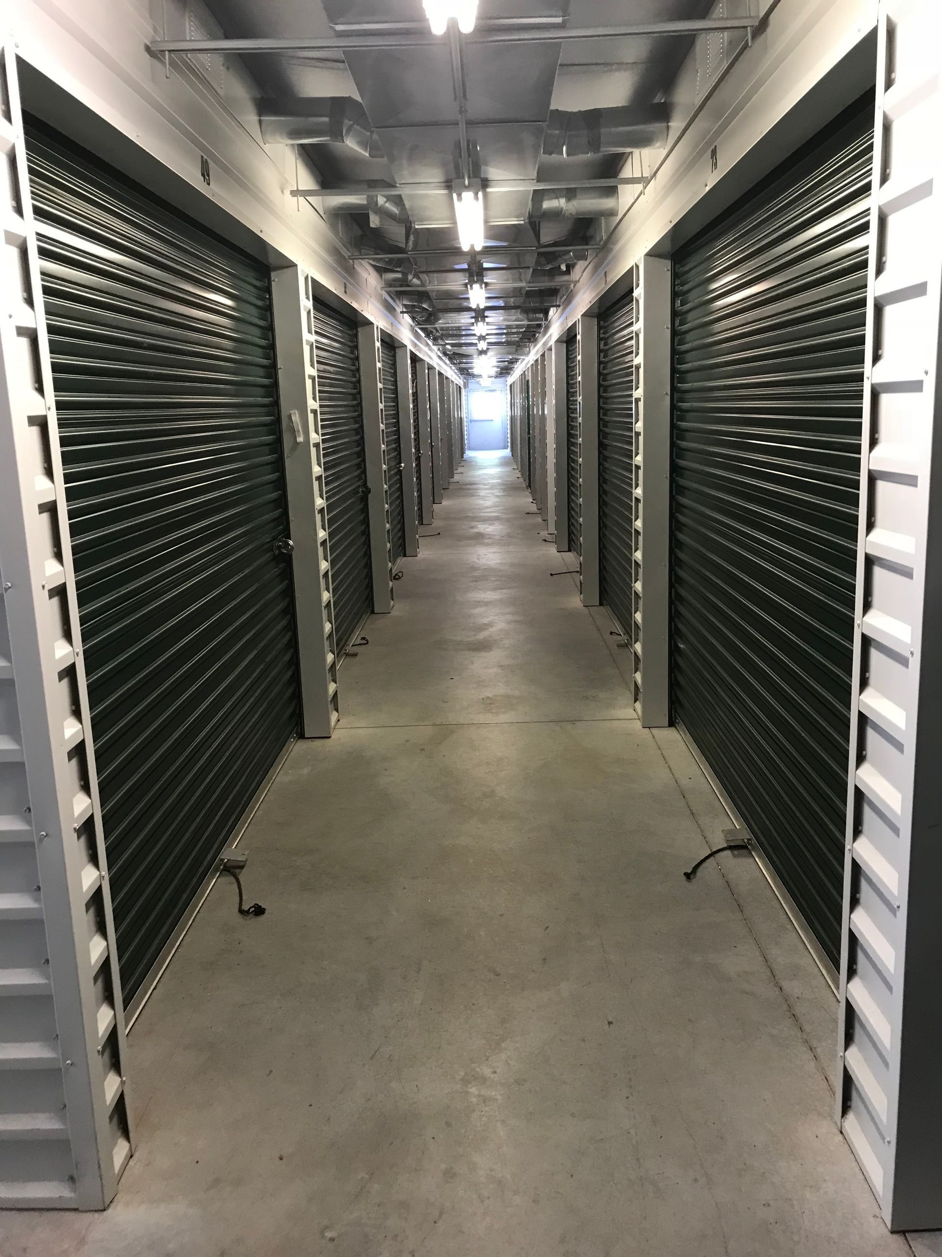 A long, narrow server room aisle with rows of black equipment racks and bright overhead lights.