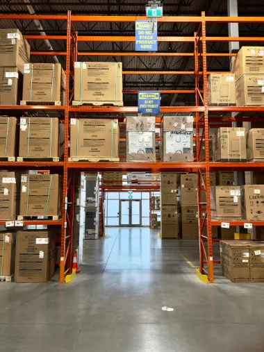 Warehouse aisle with orange pallet racks stacked with cardboard boxes and a clear walkway down the center