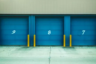 Three blue loading dock doors numbered 9, 8, and 7 with yellow bumpers on a concrete lot.