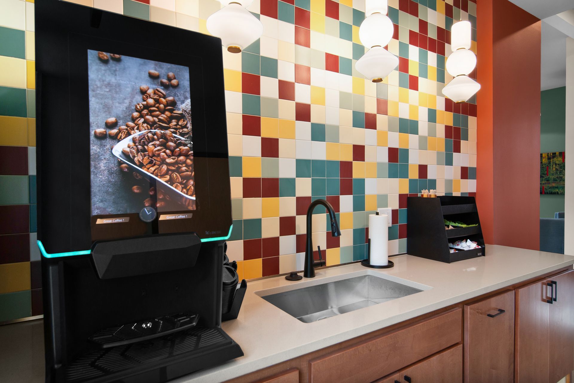 Modern lobby with coffee station, colorful tile wall, and glass double doors leading outside