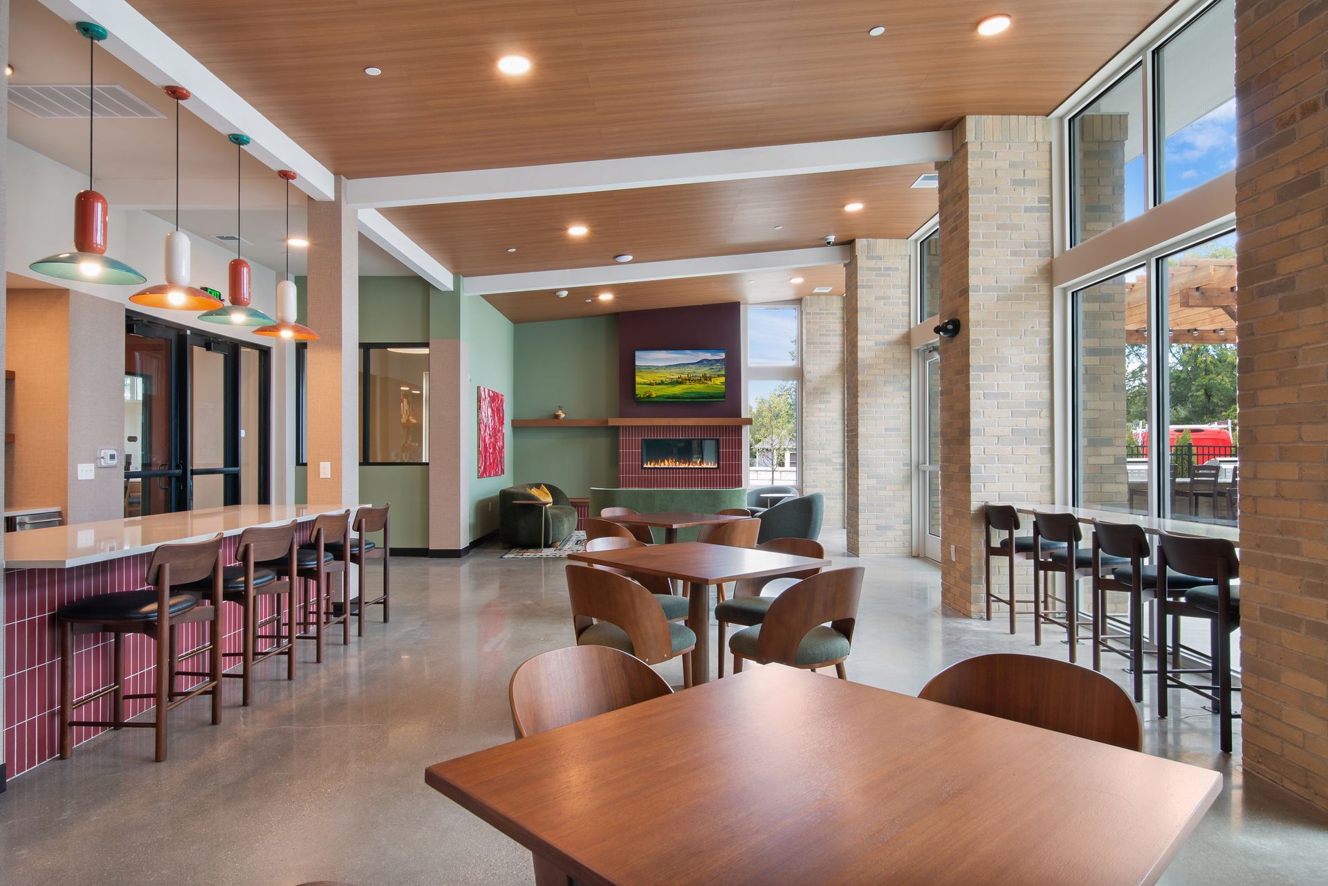 Modern lounge with tan chairs, tables, bar stools, and brick walls in a bright lobby area