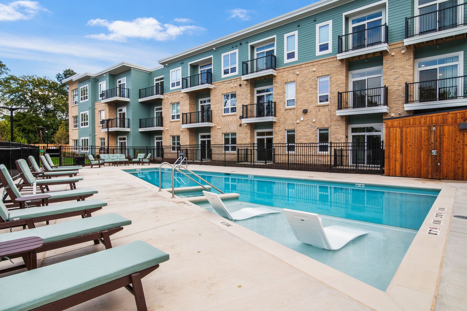 Apartment complex courtyard with a swimming pool, lounge chairs, and balconies under a clear sky