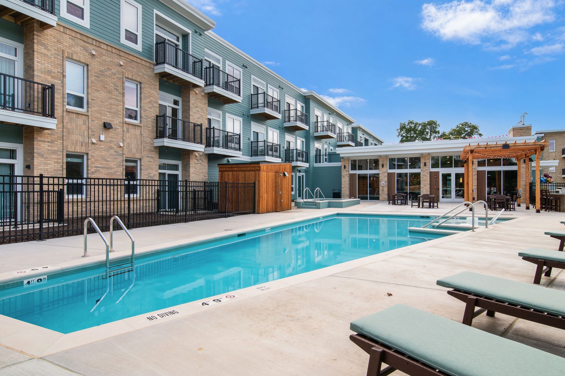 Modern hotel courtyard with a blue swimming pool, lounge chairs, and balconies in the background