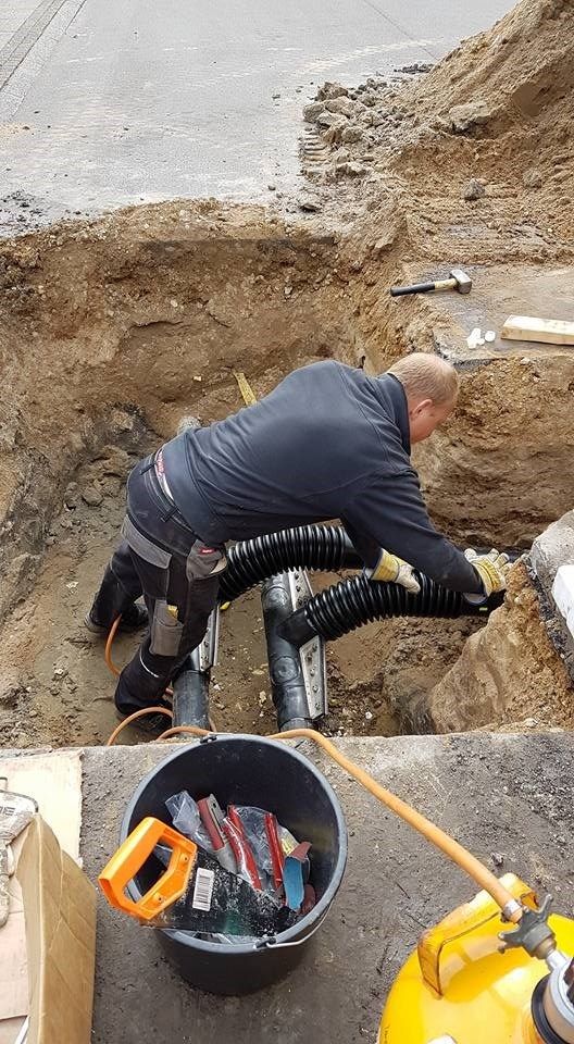 En mand arbejder på et rør i jorden ved siden af ​​en spand værktøj.