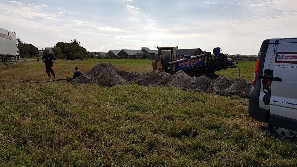 En traktor graver et hul på en mark ved siden af ​​en varebil.