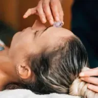A woman is getting a facial massage with a crystal on her forehead.