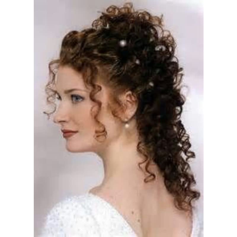 A woman with curly hair and pearls in her hair is wearing a white dress.