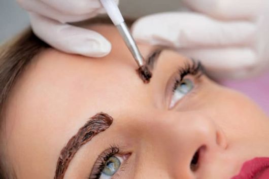 A woman is getting her eyebrows painted with henna.