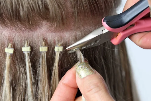 A person is holding a pair of pliers over a woman 's hair extensions.