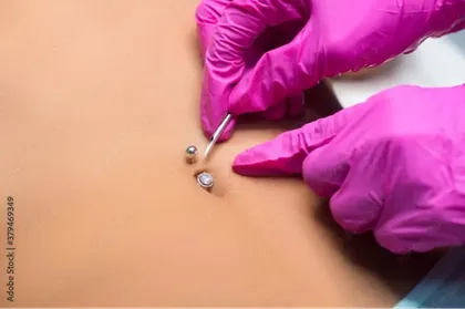 A person wearing pink gloves is piercing a woman 's belly button.