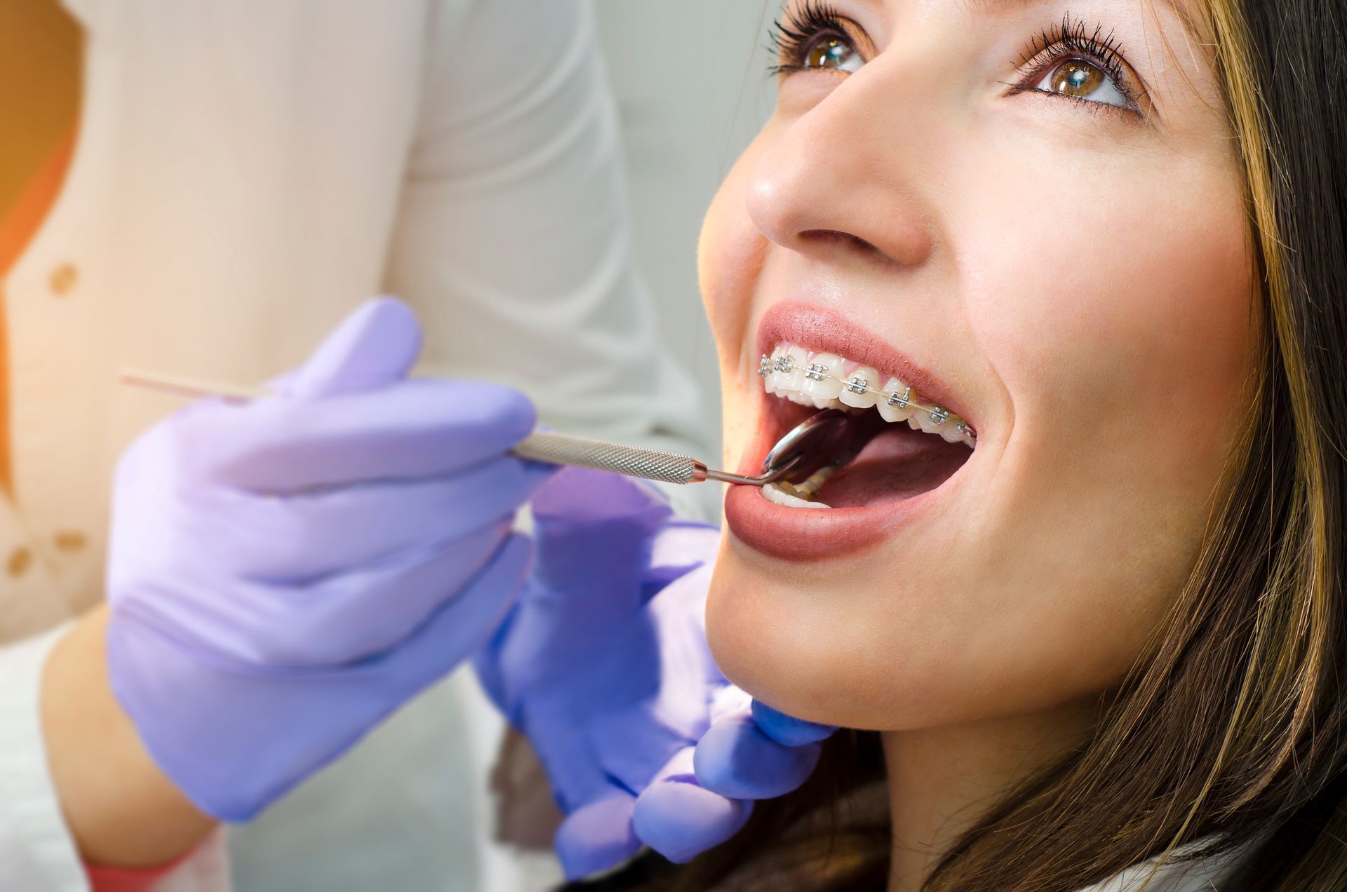 A woman with braces is getting her teeth examined by a dentist.