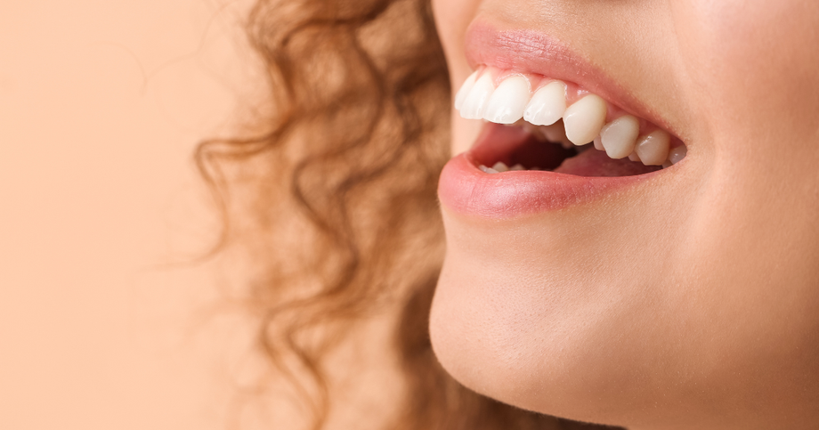 Gros plan sur une personne souriante, montrant des dents blanches, avec des cheveux bouclés visibles à gauche