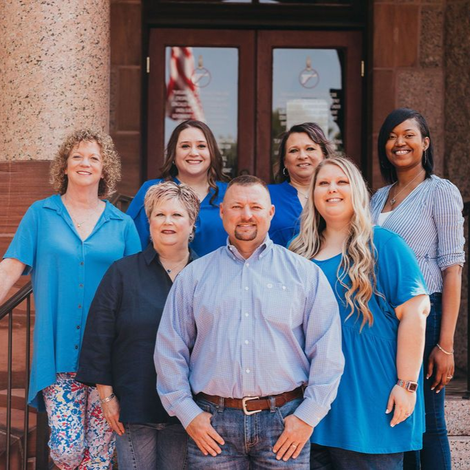 Seven people posing together in front of a building entrance, smiling at the camera.