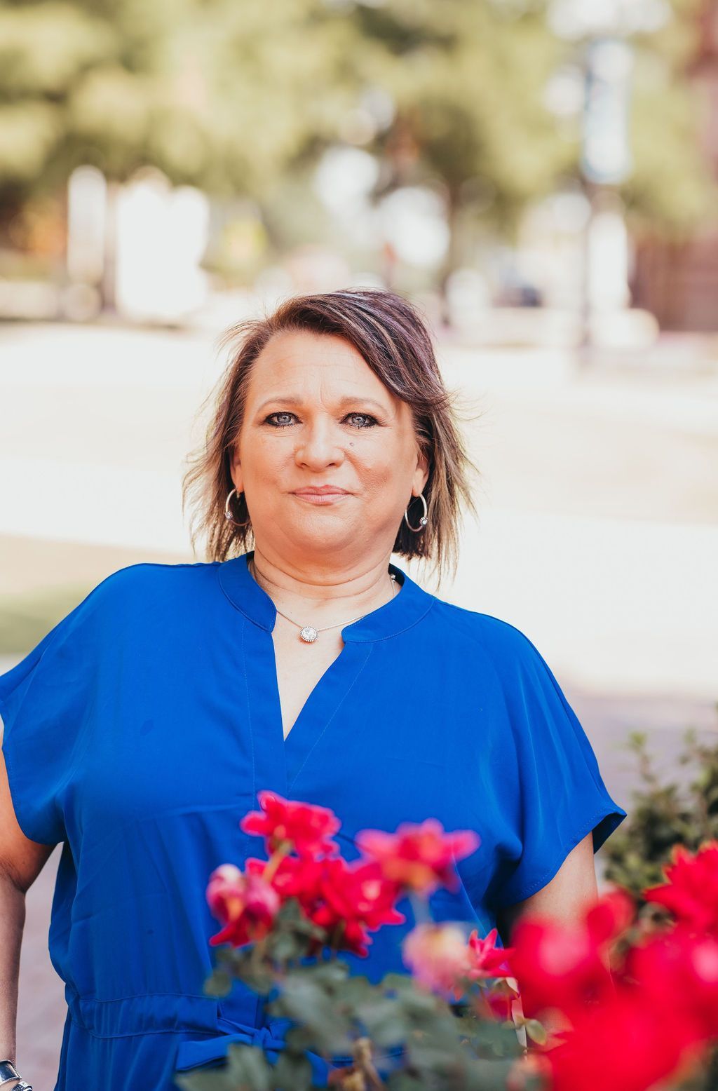 Woman in a bright blue blouse standing outdoors with pink flowers in the foreground