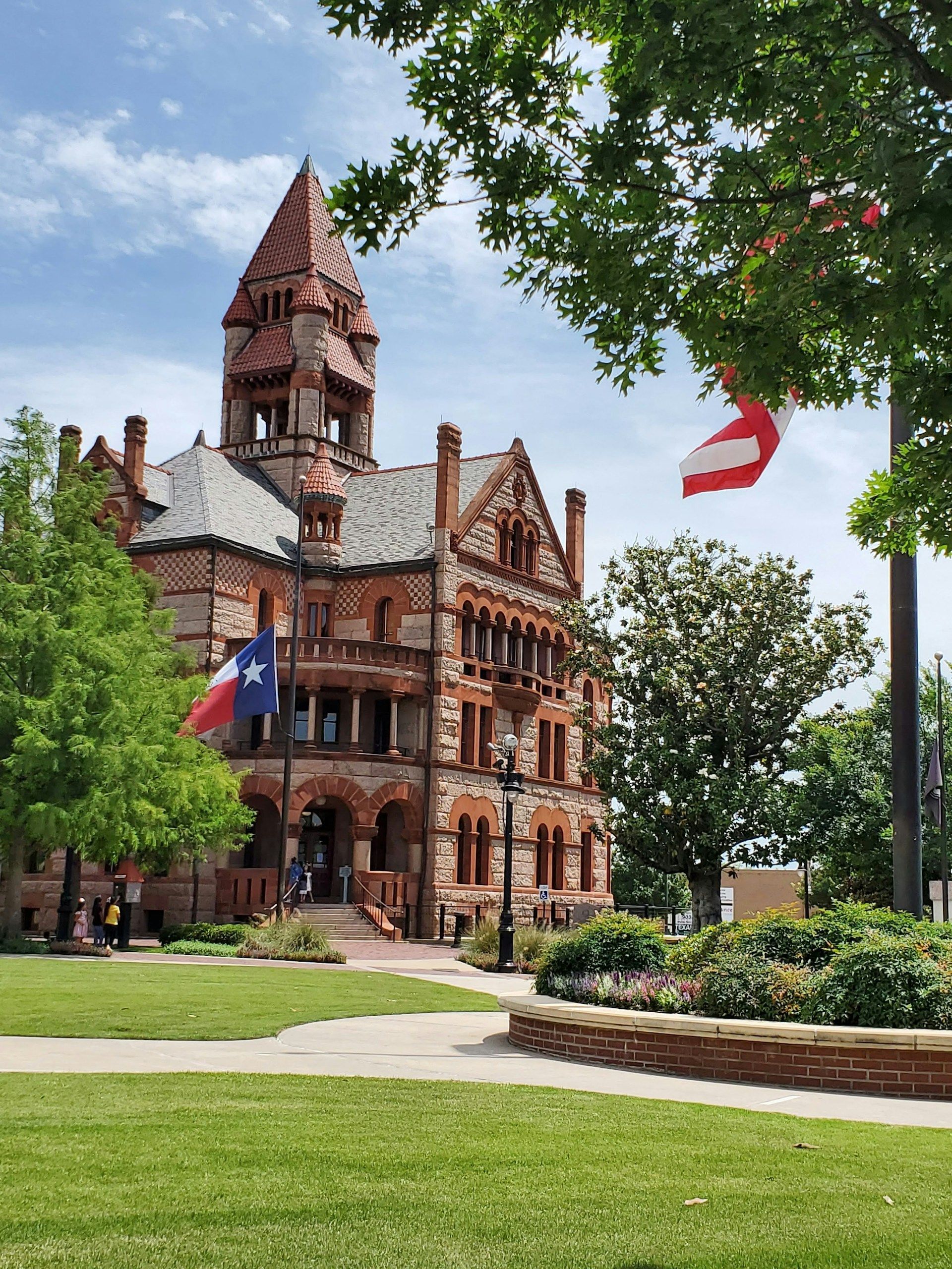 Historic red-brick building with tower, green lawn, and trees under a blue sky