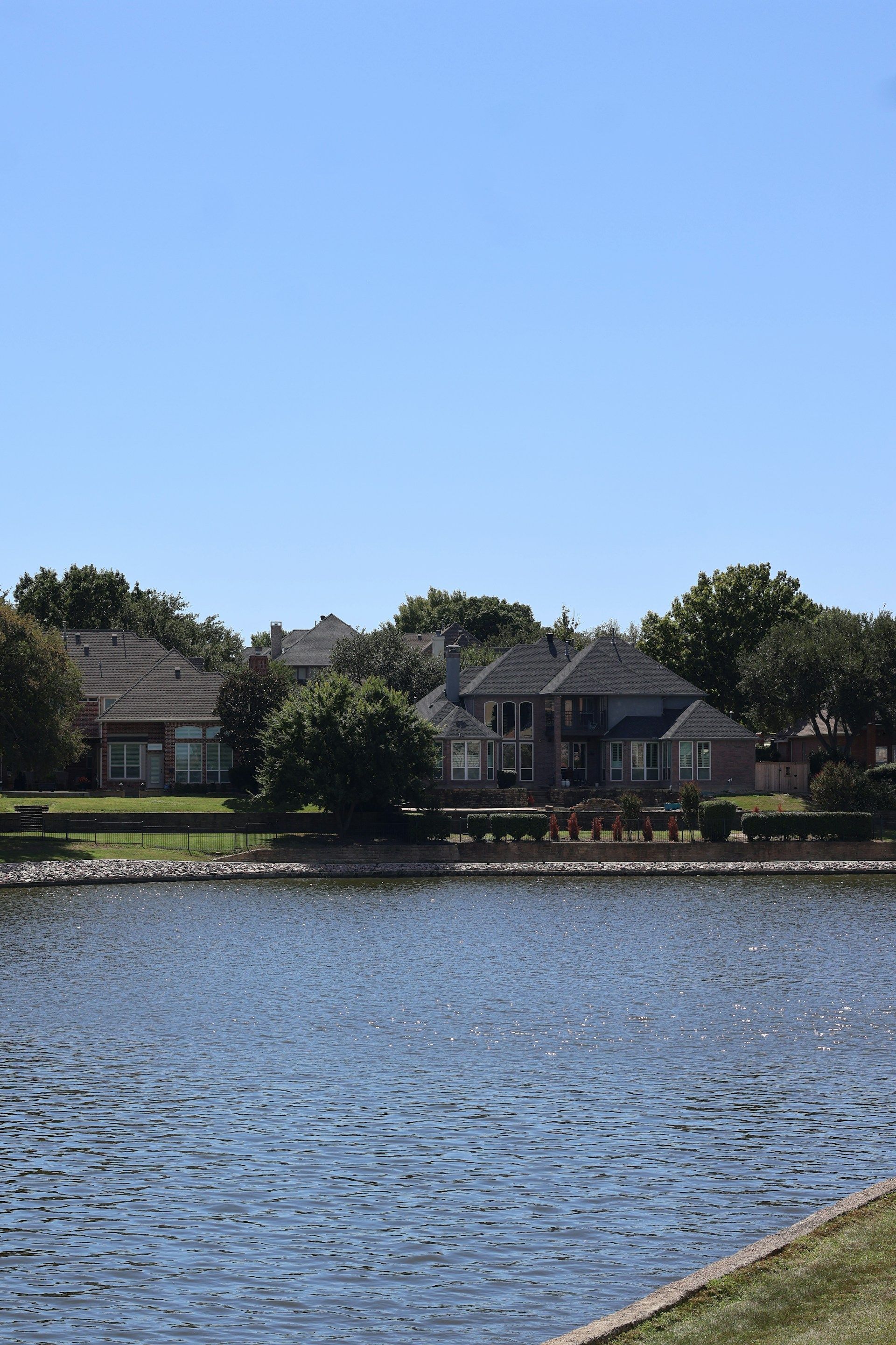 Calm lake with rippling water and houses along the far shore under a clear blue sky