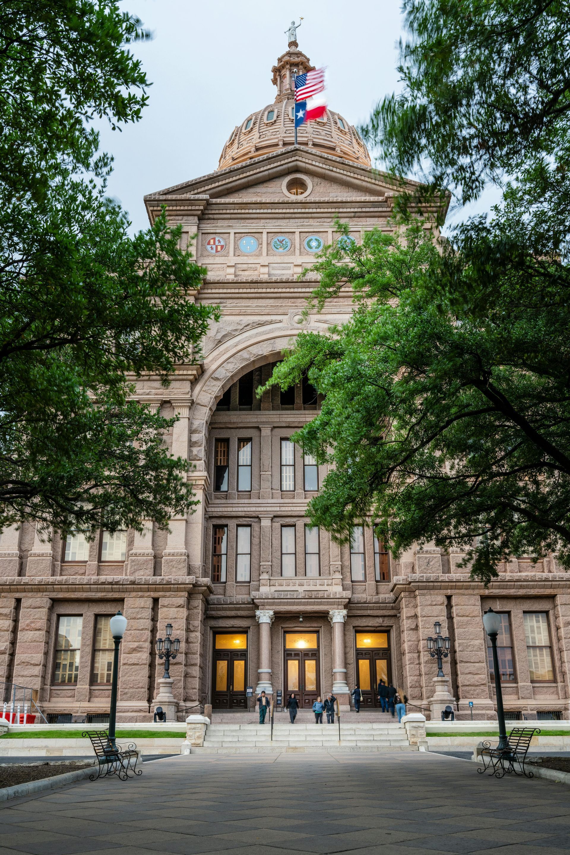 Historic stone courthouse with a domed roof and flags, framed by trees and a walkway.