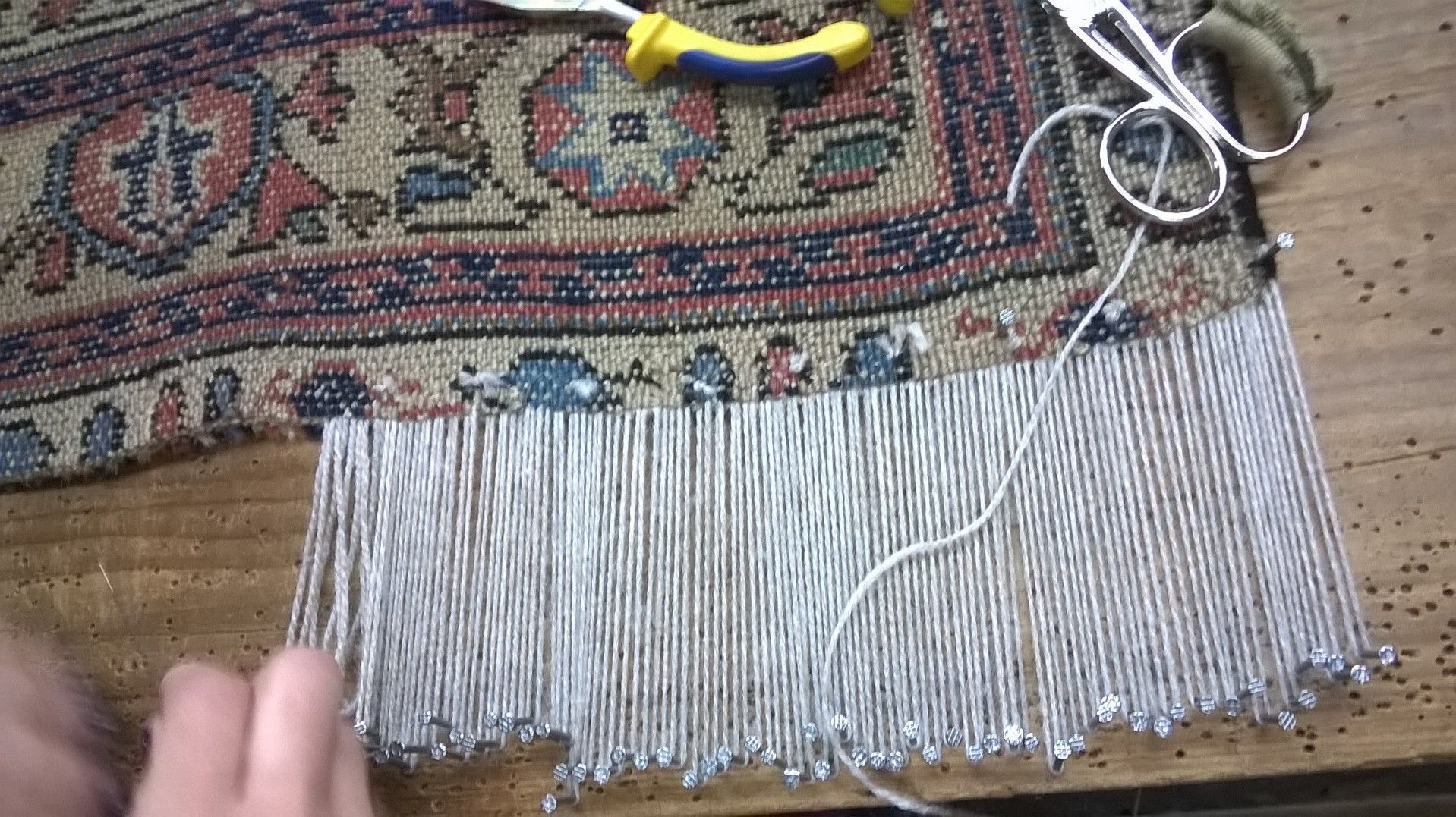 Alfombra enrollada con estampado beige y azul marino y flecos sobre una alfombra clara.