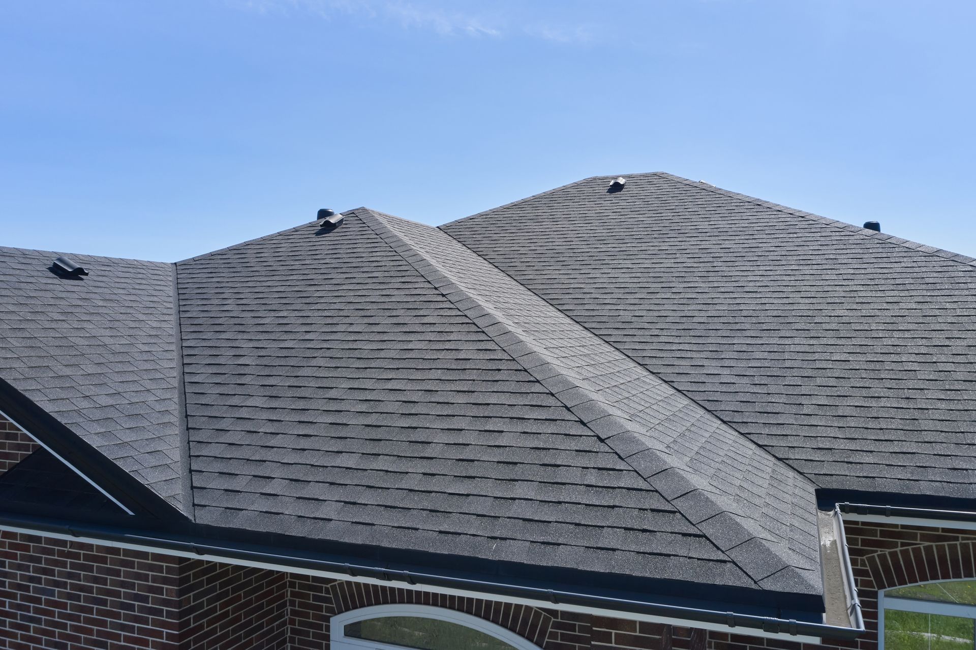 A view of a shingled residential roof with several peaks and valleys under a clear blue sky.