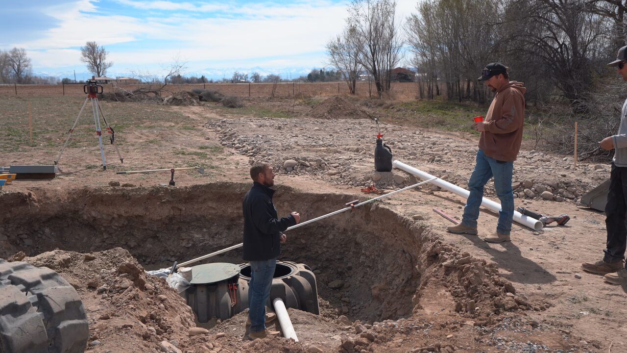 People working near an open trench in a dry field, lifting a long white pipe.
