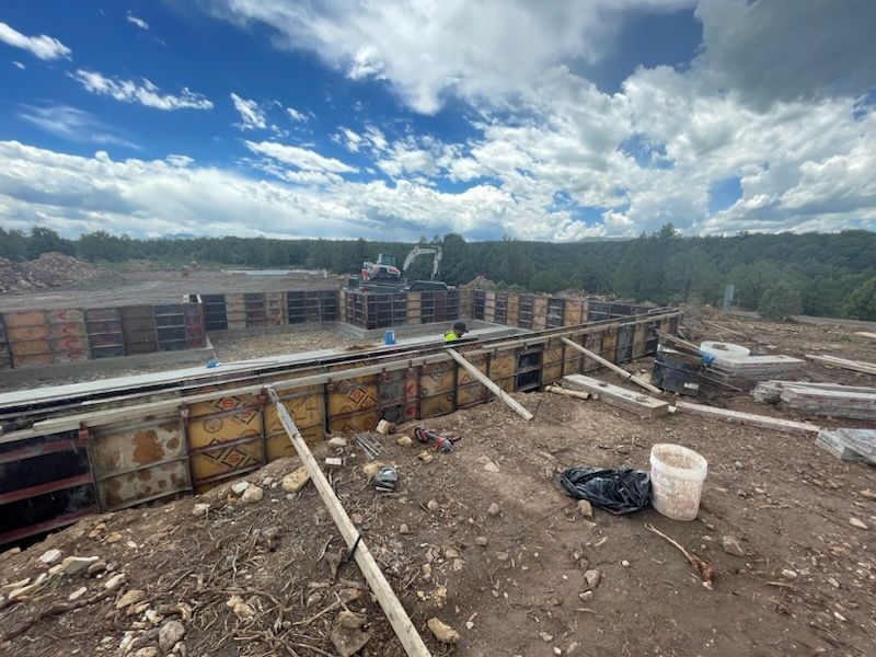 construction site with concrete walls, pipes, debris, for a foundation and a cloudy sky over a wooded horizon