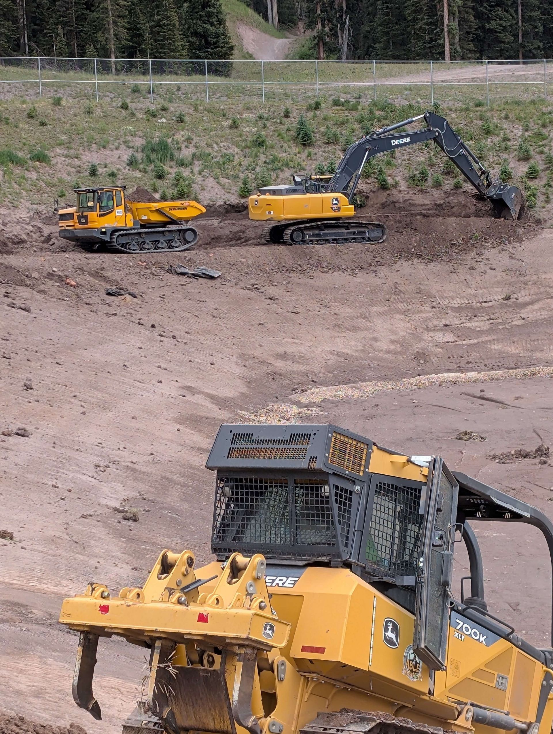 Yellow excavators and a bulldozer working in a dirt quarry with a steep hillside background