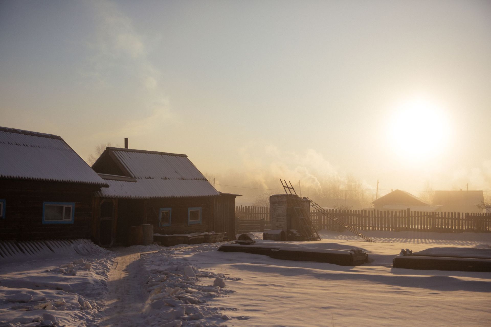 Snow-covered rural backyard with wooden outbuildings at sunrise on a frosty winter morning