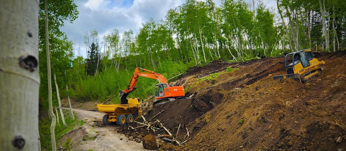 Excavator and dozer clearing a steep forested hillside in Western Colorado