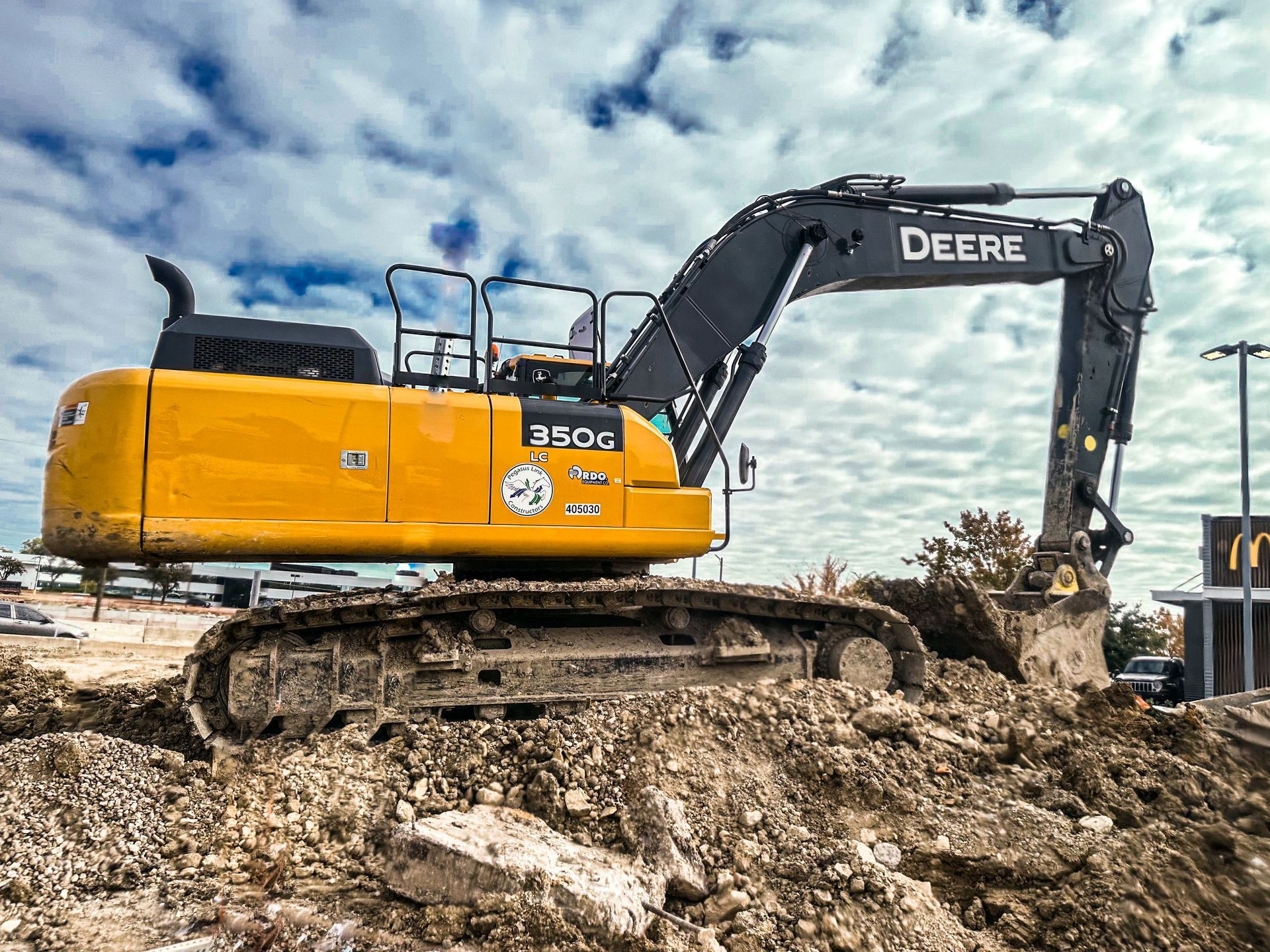 Yellow and black John Deere excavator on a muddy construction site under a cloudy sky