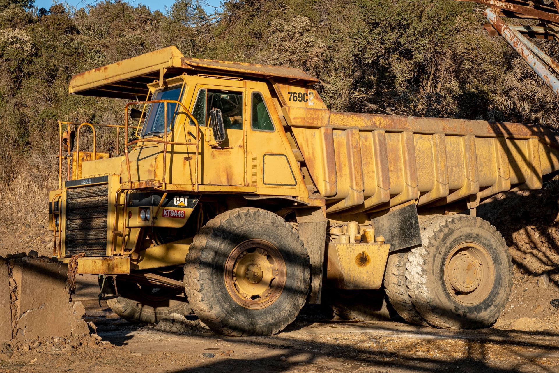 Yellow dump truck driving on a dirt road in a dry, rocky landscape